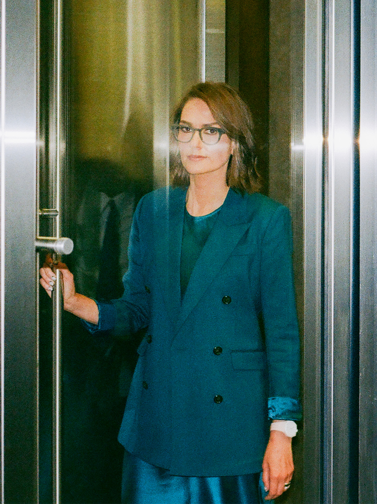 Jessica Tarlov stands in a revolving doorway wearing a teal pantsuit and glasses.