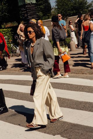 A woman at Copenhagen fashion week wearing a plaid blazer, white trousers, and brown sneakers