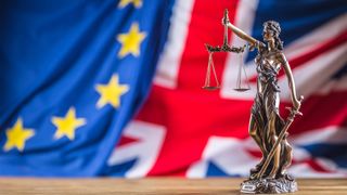 Lady Justice, symbol of law in front of EU and UK flags.