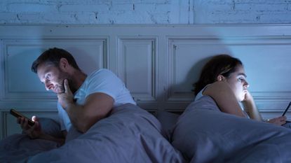 Young couple in bed late at night using smart phones obsessed with games, social media and apps ignoring each other in relationship communication prob
