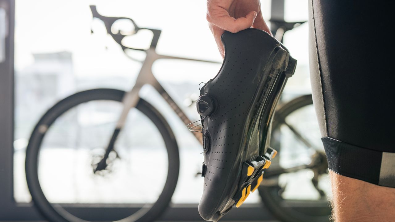 The best indoor cycling shoes shows a black pair being held with a bike in the background