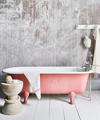 bathroom wall painted to look like plaster with grey chalk paints behind a pink painted bath