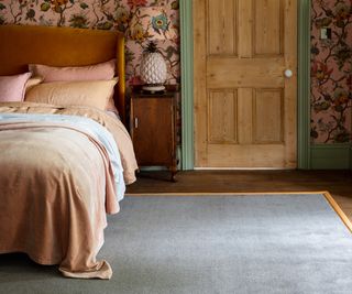 bedroom with wooden door and floor, grey rug, pink and green patterned wallpaper