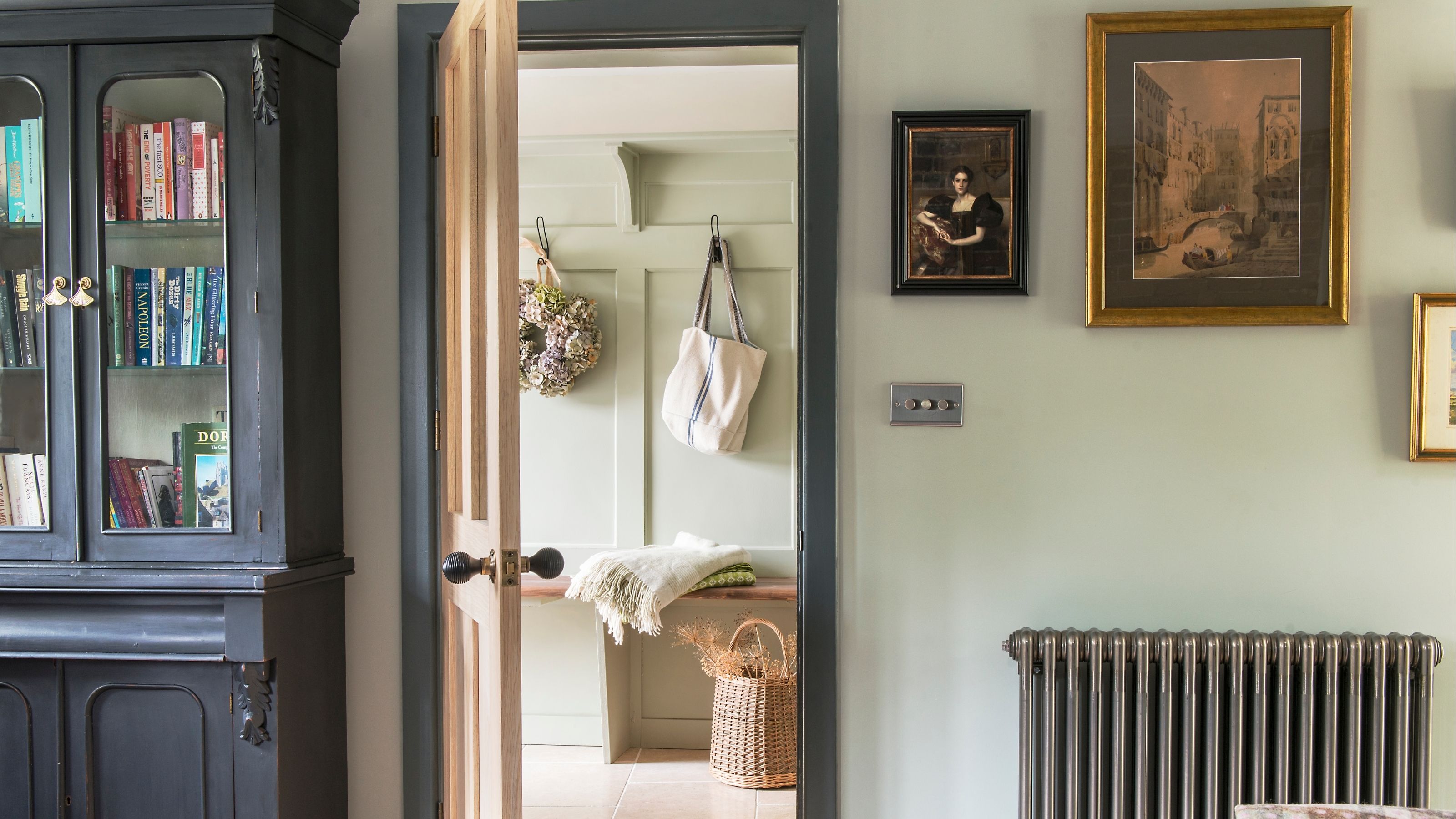 A traditional, vintage-style, pale green hallway adorned with gold frames, and antique home decor. 