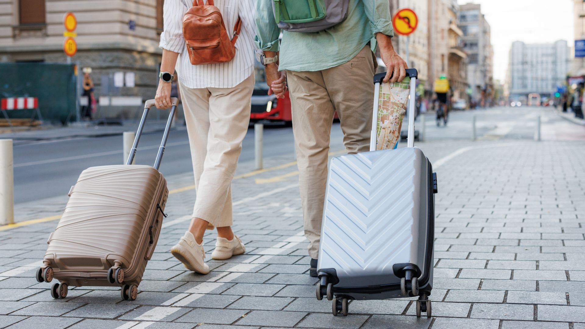 A man and woman walk down a city street with their luggage.