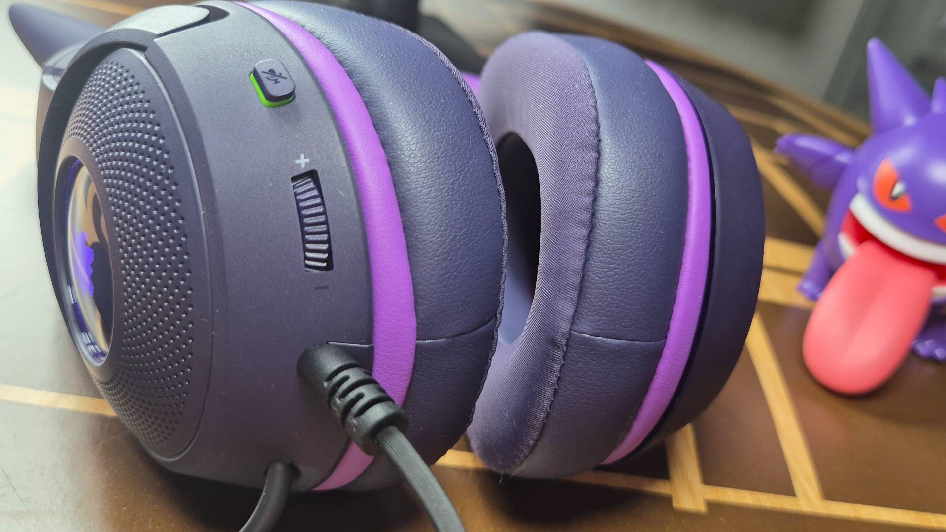 Photo of the edge of the cups of a purple headset, with a toy of the Pokemon Gengar in the background.