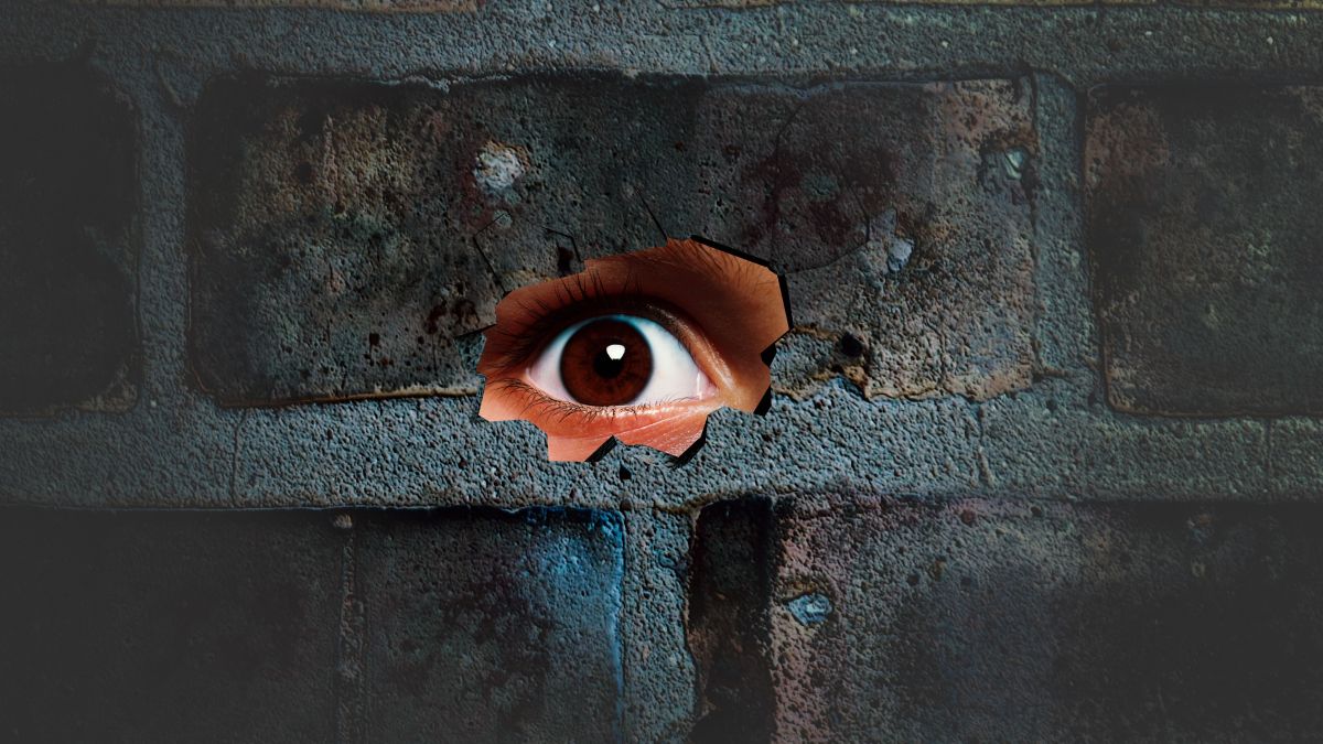 Eye looking through the hole on cracked wall. Spy peeking through hole in brick wall. Spy concept.