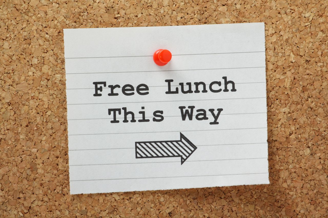 Notepaper with &quot;Free Lunch This Way&quot; written on it pinned to a corkboard