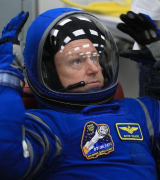 an astronaut raising his hands in a spacesuit beside his closed helmet visor