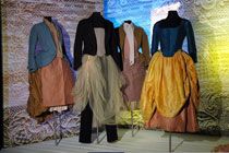 Four black, headless mannequins displaying dresses and jackets in blue, brown, black, cream and mustard colours against a patterned background