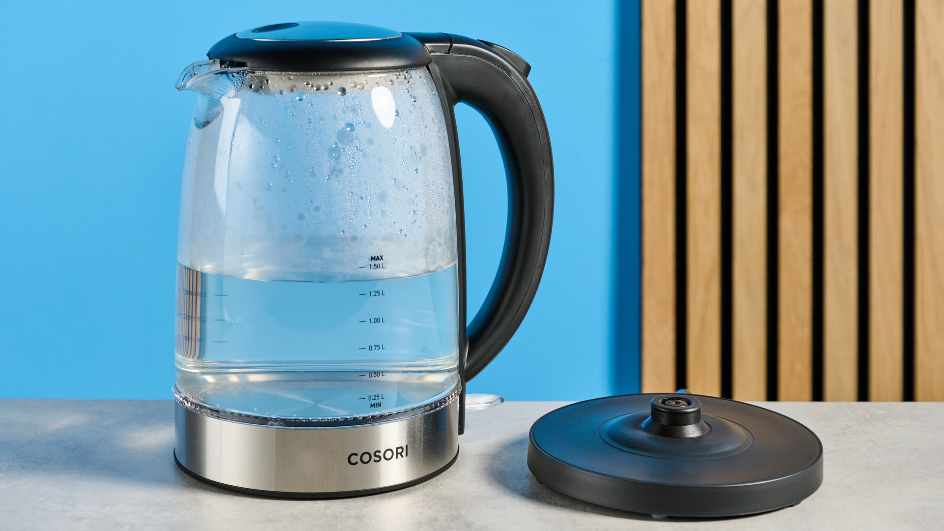 Cosori Electric Glass Kettle photographed in front of a blue background.