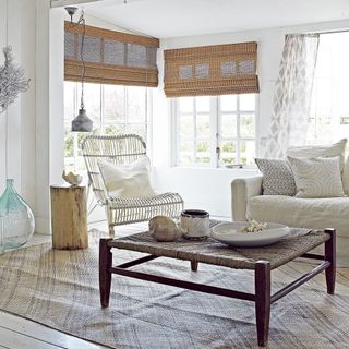 a neutral living room with a coastal touch, with bamboo blinds and chair, woven coffee table and linen cover sofa
