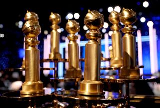 A collection of Golden Globes trophies displayed on a table in front of a stage