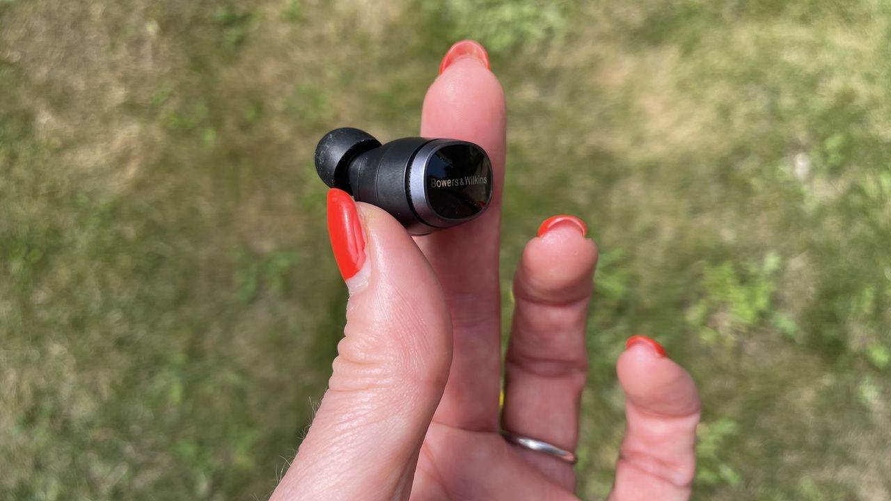 Bowers &amp; Wilkins Pi8 earbuds, held in a hand on grassy background