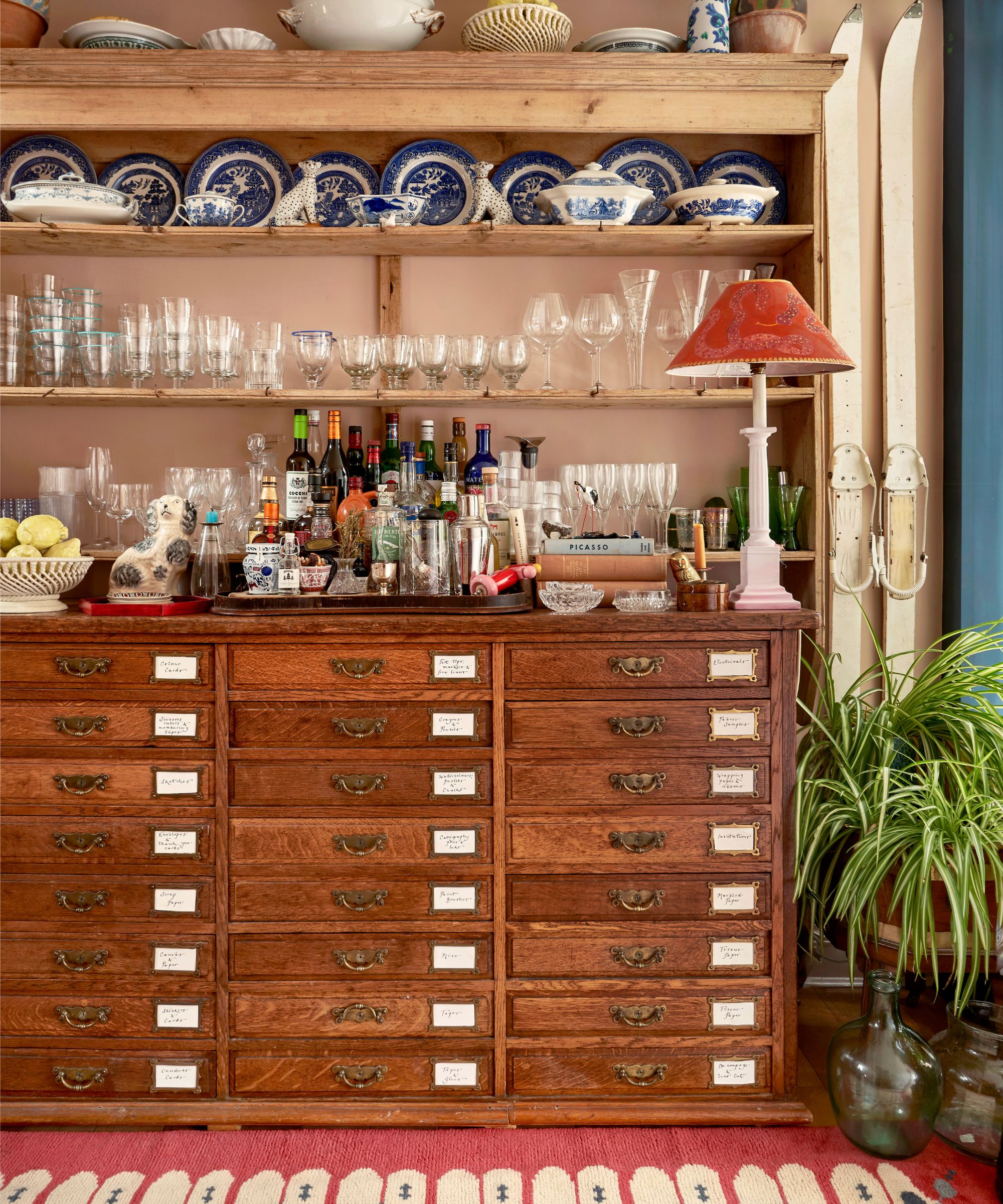 Antique dresser with china plates, glassware collection and bar accessories, lamp and pink rug