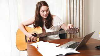 Close-up of a woman playing acoustic guitar at a laptop
