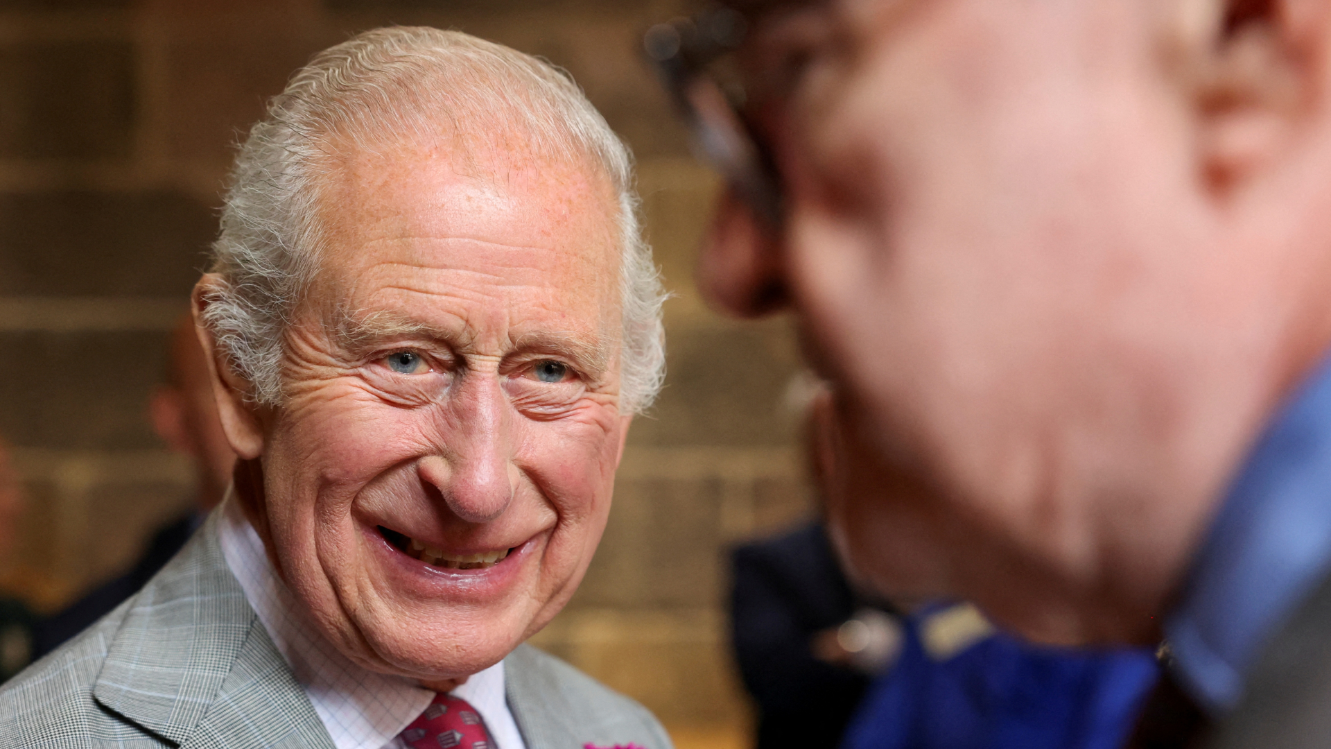 King Charles in a gray suit smiling at a D-Day veteran