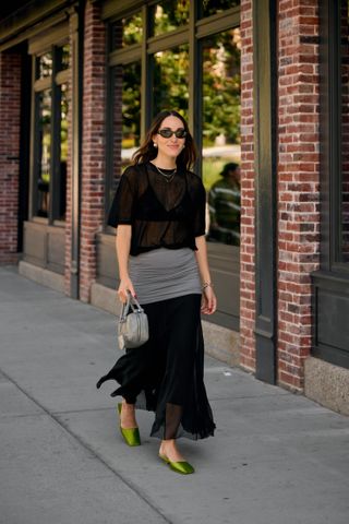 Anna LaPlaca wearing a St. Agni sheer t-shirt, Tory Burch sheer and ruched skirt, grey crinkled leather Prada handbag, and green satin Prada mules