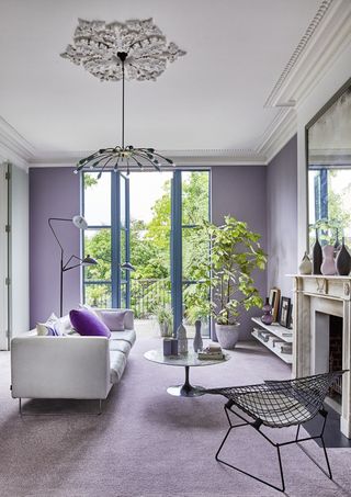 living room with lilac carpet and walls, white couch, metal armchair, plants, round coffee table, floor lamp