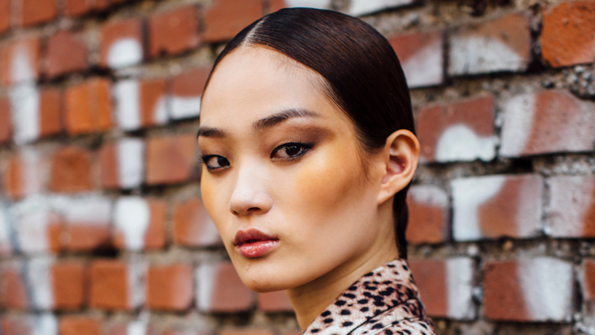 A model with bronzed skin and a low slicked back bun.
