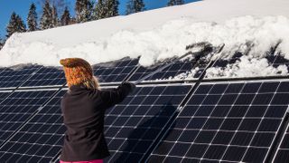 Woman clearing snow with broom from rooftop solar panels