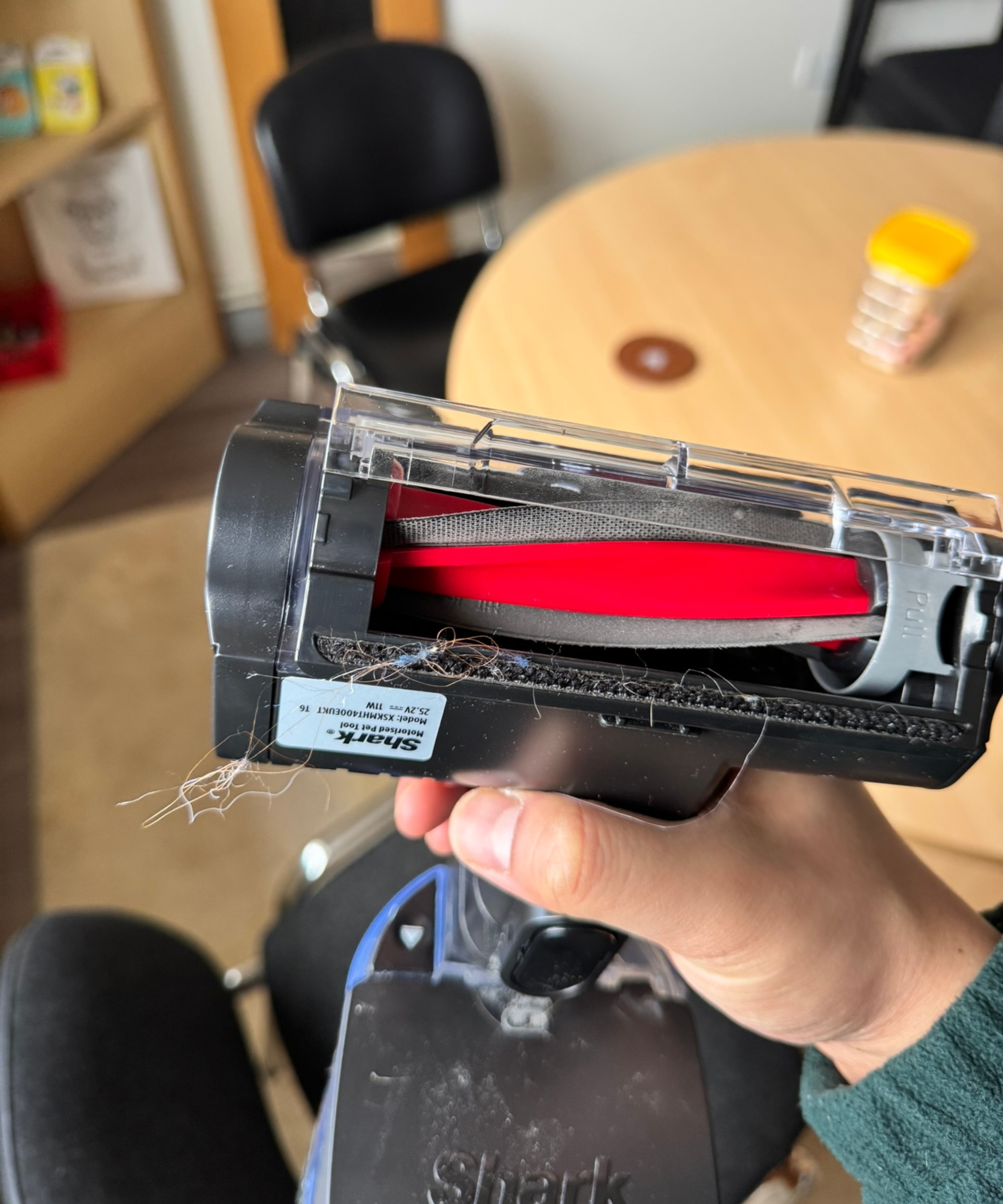 Hand holding the Shark Stratos Cordless in handheld mode, upside down to reveal the roller with fur and thread coming out.