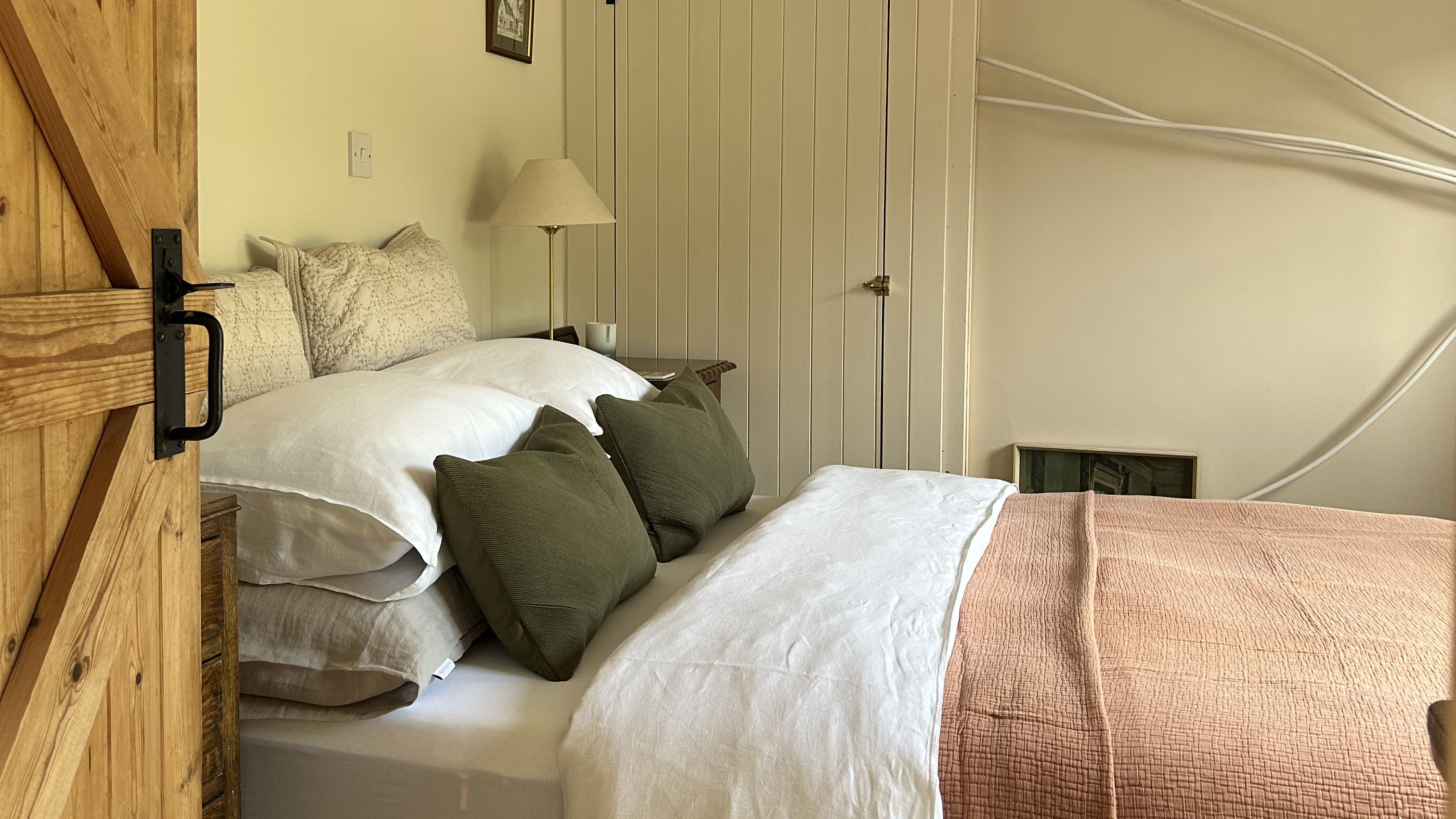 a bedroom with a beautifully-made bed even though wires still hang on the wall next to it mid renovation