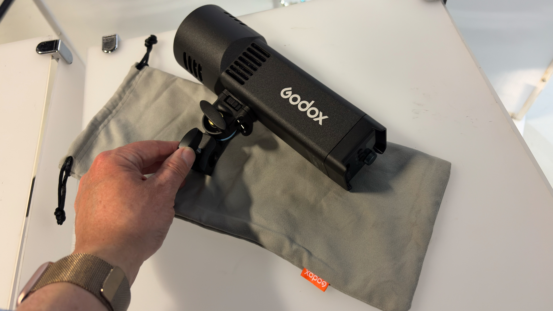 Shot of a hand touching the supplied AD-E2 holder, which is attached to the Godox RS100Bi. The supplied grey cloth bag sits next to the LED.