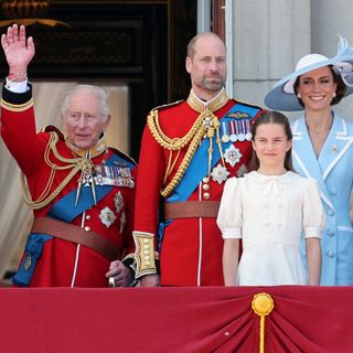 King Charles waves from the Buckingham Palace balcony while wearing a red military uniform