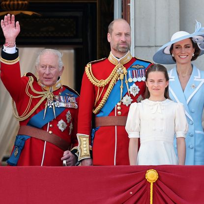 King Charles waves from the Buckingham Palace balcony while wearing a red military uniform