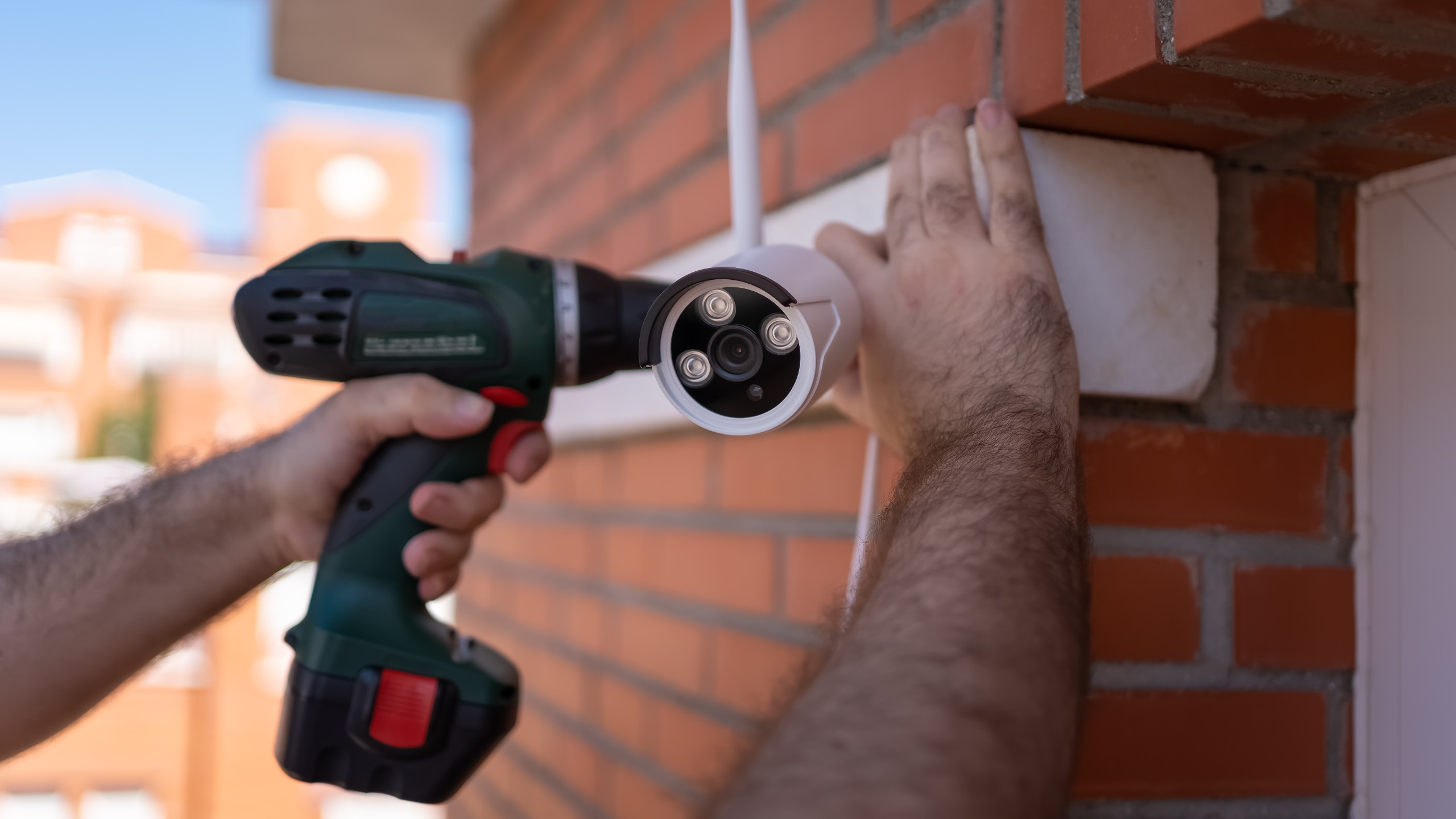 Person using a power drill to attach home security camera to exterior wall of house