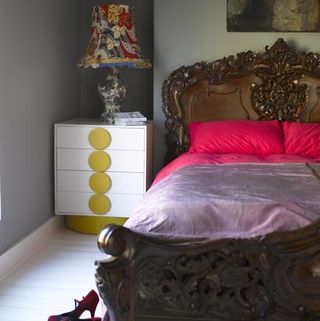 bedroom with white wall and wooden bed with pink pillows and design table lamp.