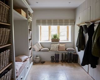 Living room in modern country home, limestone flooring, bench seating, tall shelving with storage baskets, coat racks, boots on floor