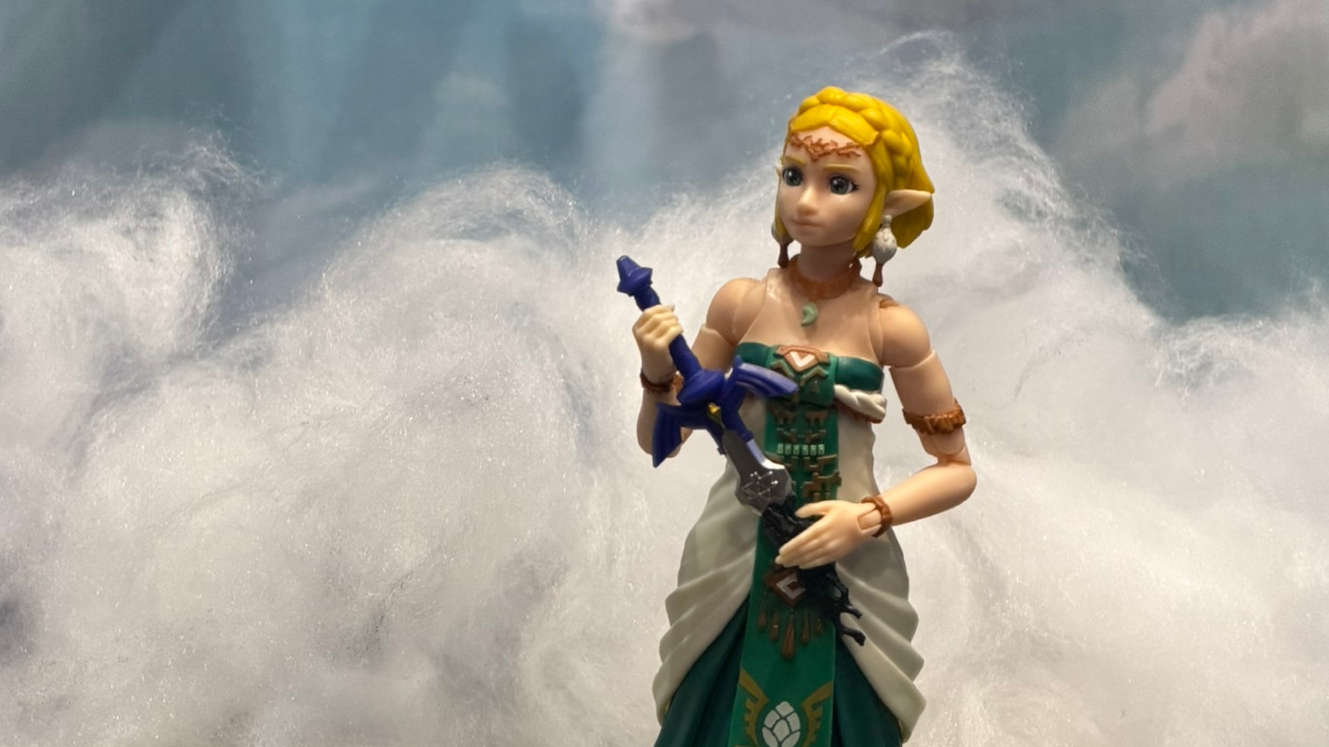 A Princess Zelda action figure against a cloudy background, holding a broken Master Sword