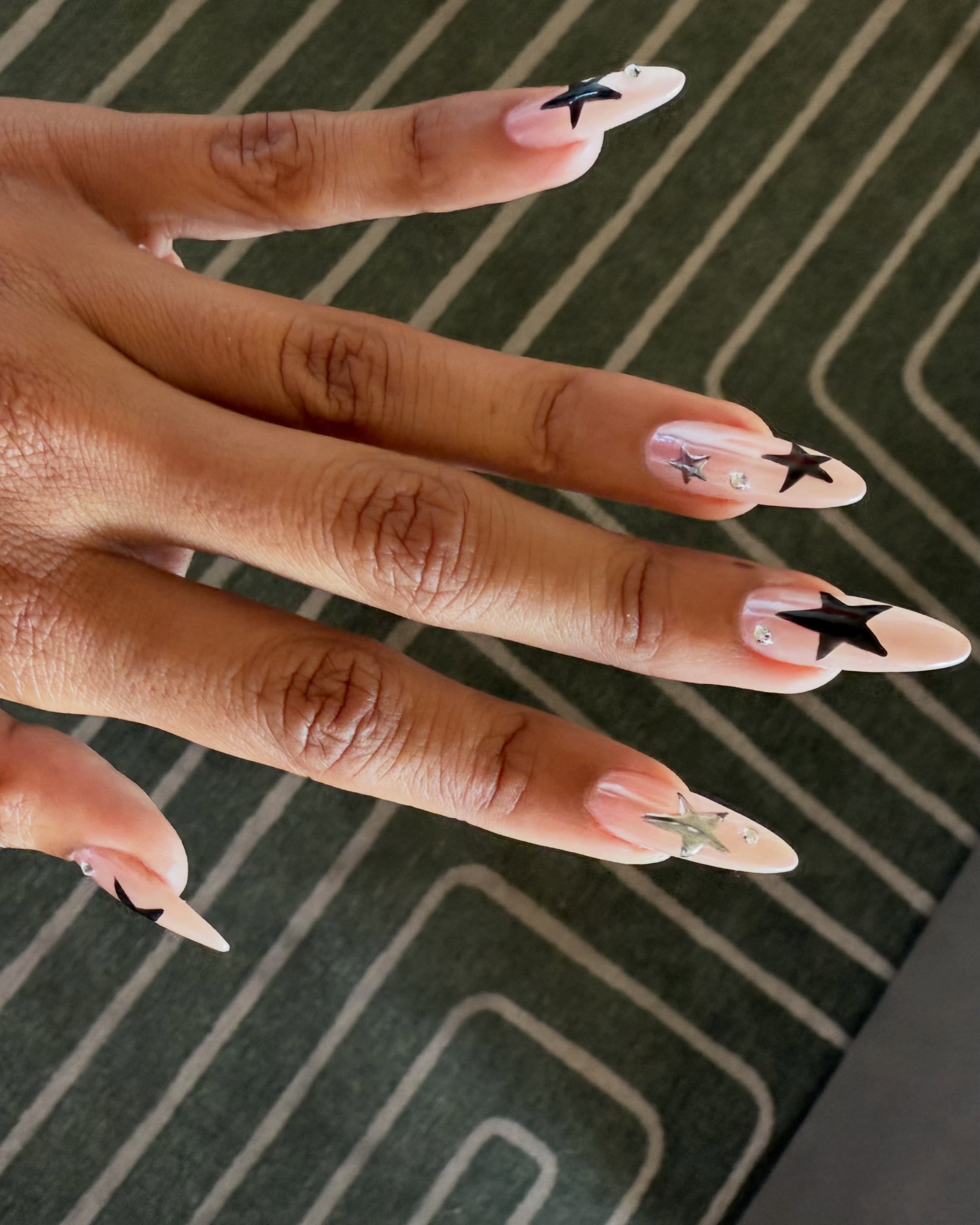 Long almond nails with a sheer pink base, large black stars and silver accents