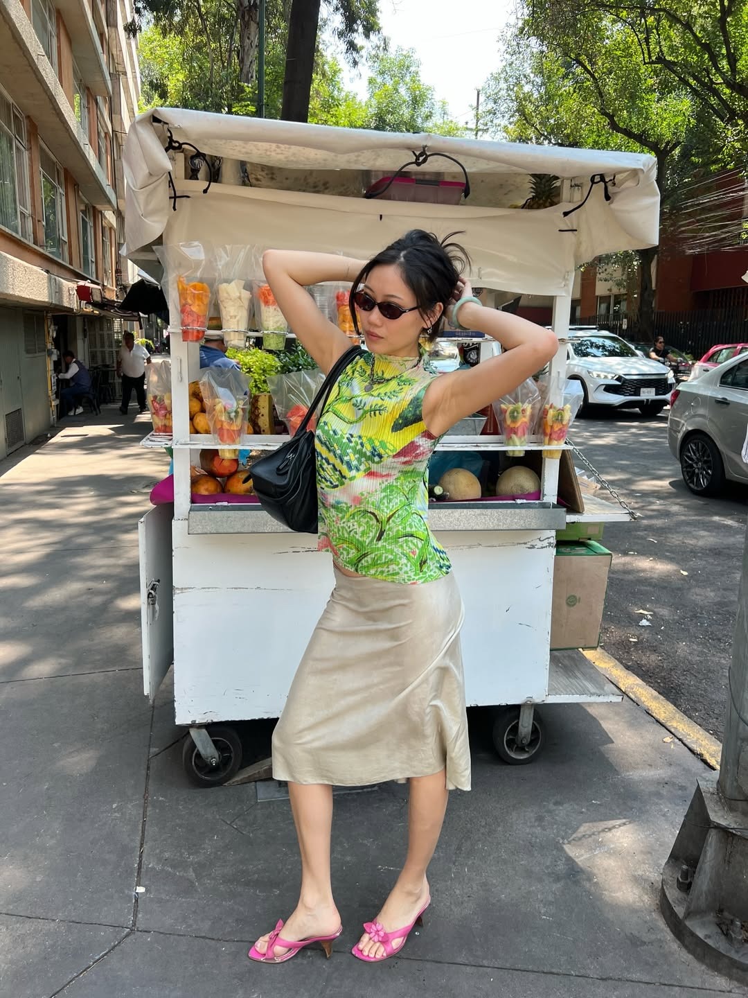 Woman in a print top, beige skirt and pink heels.