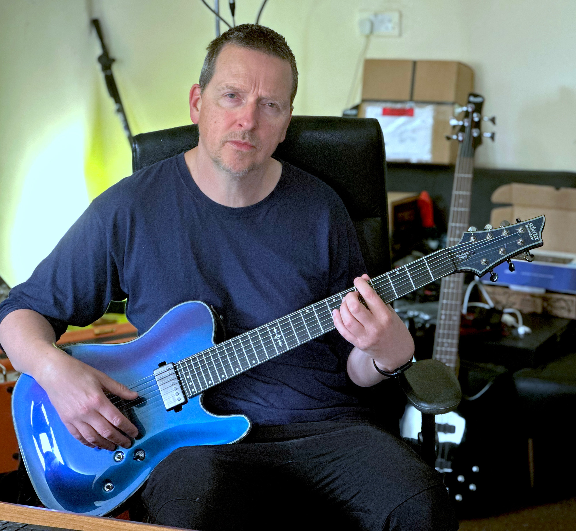 Justin Broadrick poses in his home studio with a Schecter seven-string electric guitar