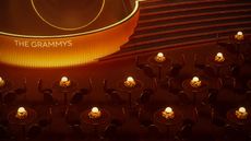 A digital rendering of a dimly lit, orange-tinted ceremony room with round tables, sculptural chairs, and lamps as centerpieces surrounded by flowers and a stage that reads "THE GRAMMYS".