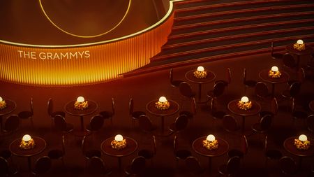 A digital rendering of a dimly lit, orange-tinted ceremony room with round tables, sculptural chairs, and lamps as centerpieces surrounded by flowers and a stage that reads "THE GRAMMYS".