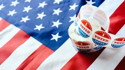 A roll of I Voted stickers sits, lightly unfurled, atop an American flag