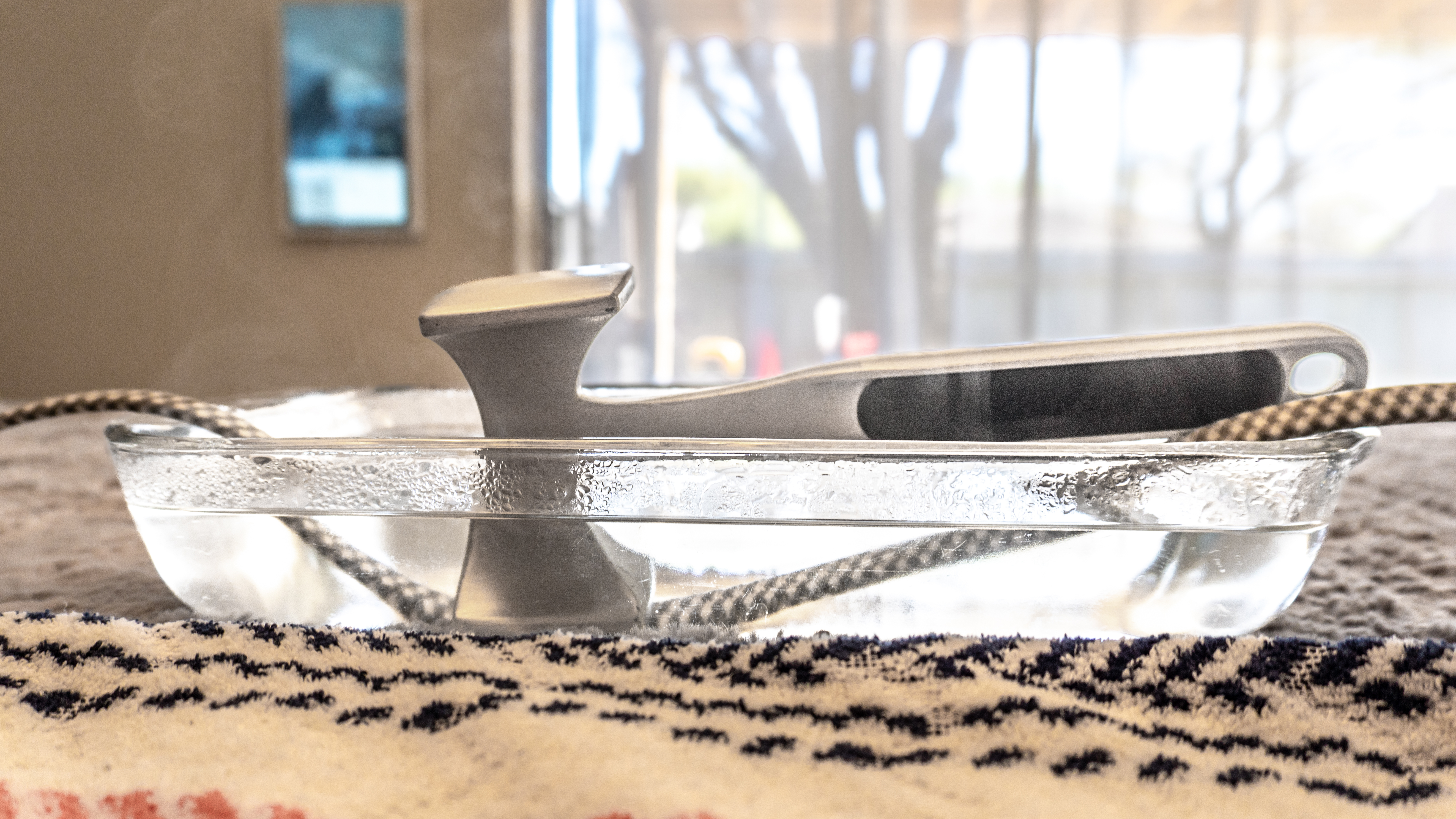 A braided surge protector cable submerged in water with a metal kitchen mallet holding it down