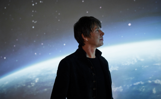 Physicist Brian Cox with picture of Earth and sky behind