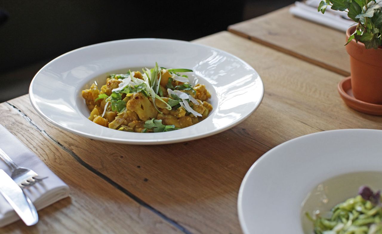 White bowl on a wooden table with potato and cauliflower curry