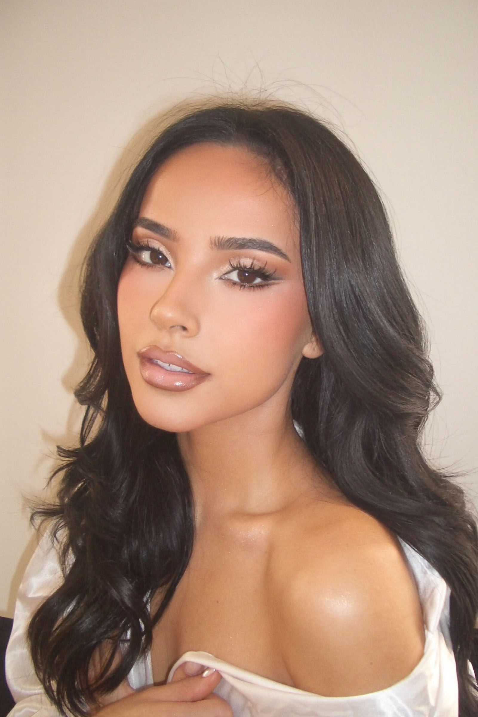 Becky G wearing an off-the-shoulder white silk robe and glam makeup.