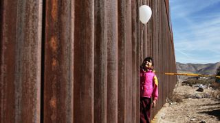 A little girl holds a white ballon at the border wall between Mexico and the United States