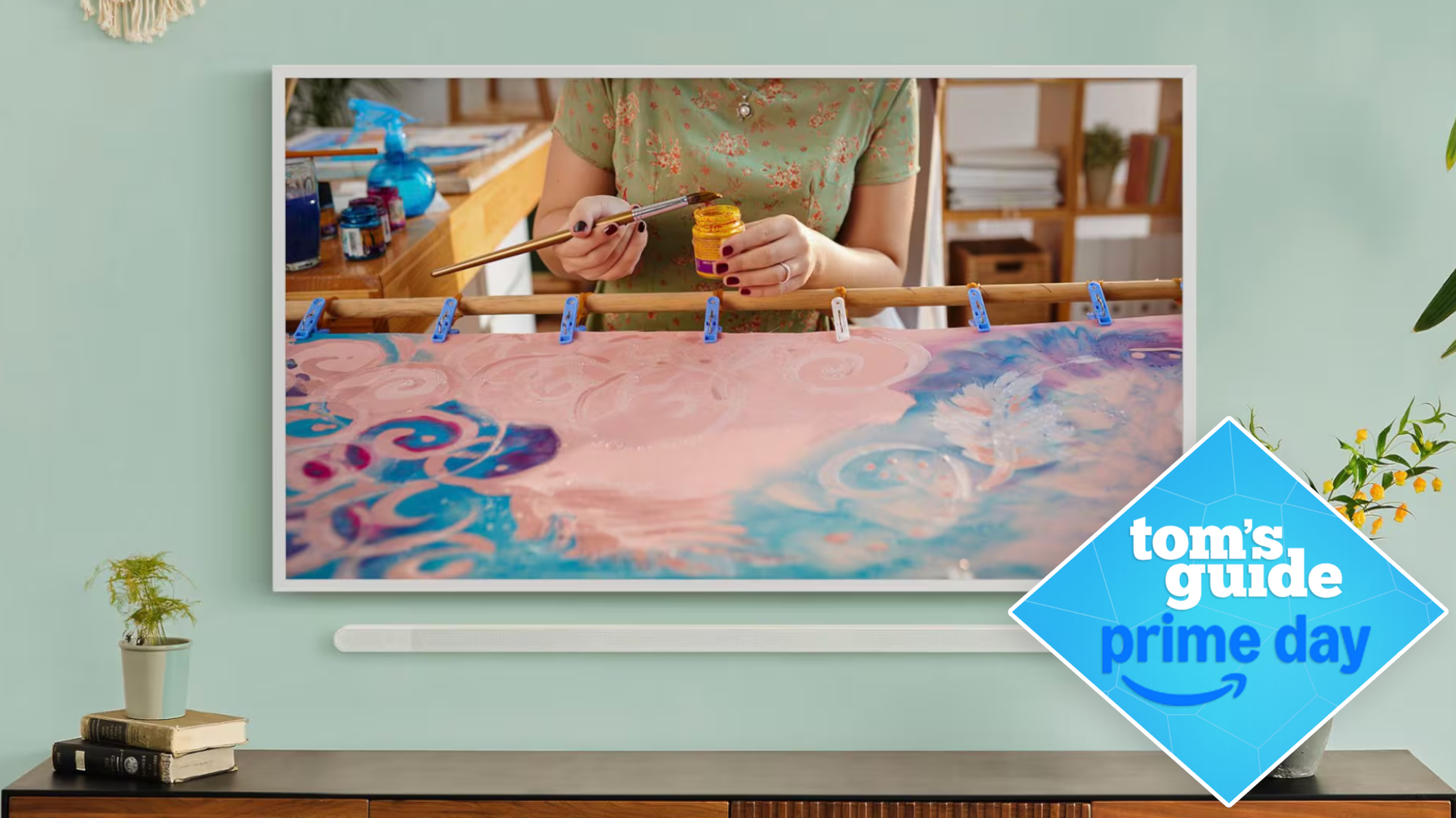 Samsung's The Frame TV wall-mounted in a living room setting. To the right of the wall-mounted TV is a badge that reads: "Tom's Guide Prime Day."