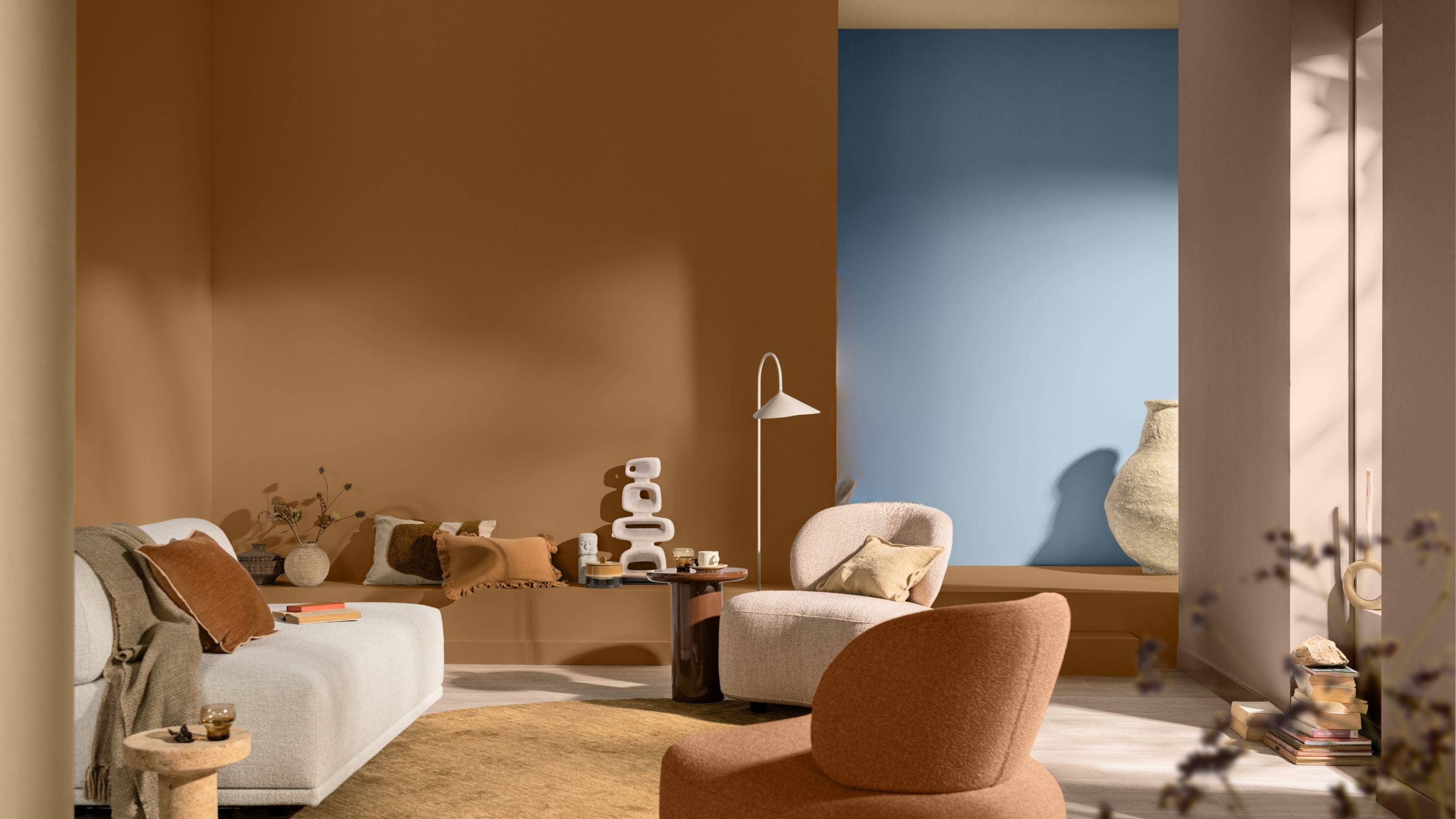 Image of a burnt orange living room with modern white seating pieces and a long and low built-in bench on the back wall that extends into a step leading to the hallway, which is painted light blue.