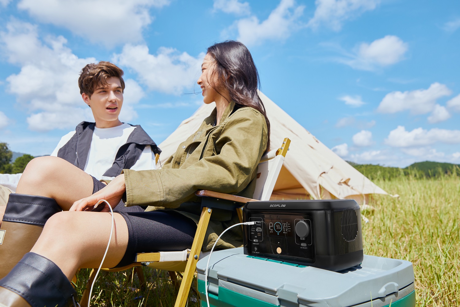 A young man and woman sitting on a blanket outside, with a tablet computer and an EcoFlow RIVER mini Portable Power Station in front of them.