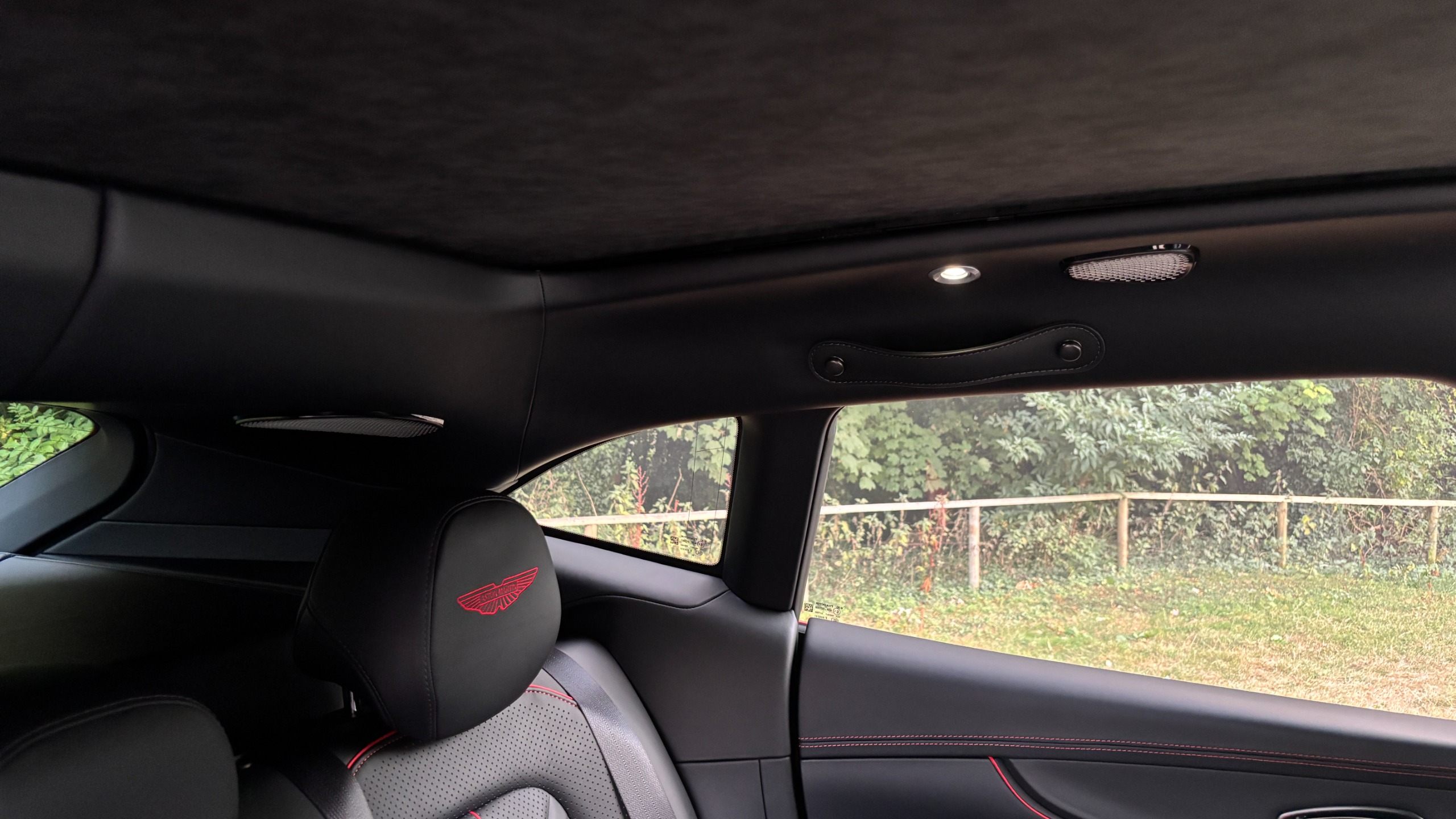 Two speaker grilles in the roof lining of an Aston Martin DBX S, above a head rest with the Aston Martin logo stitched into it