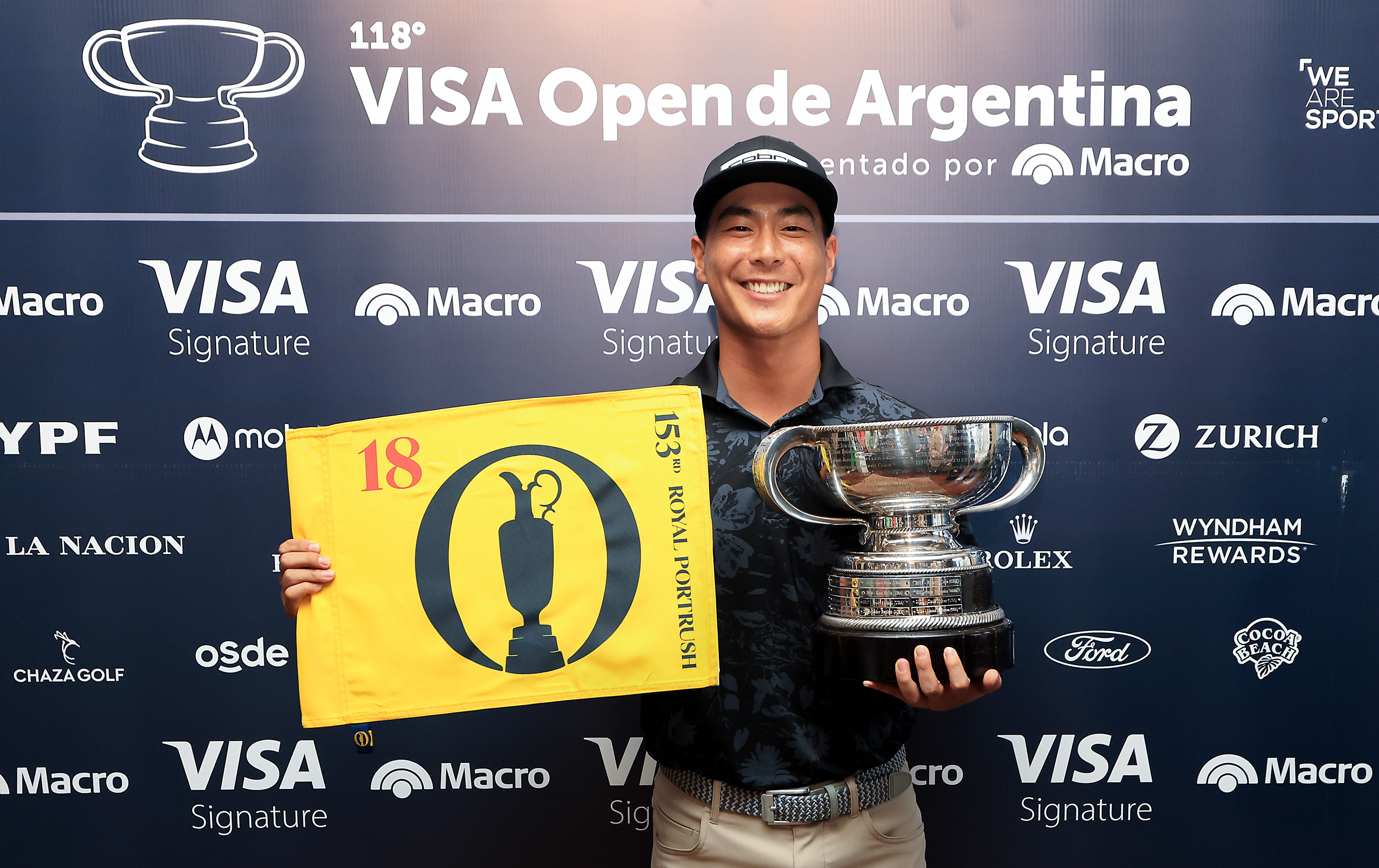 Justin Suh holding a yellow Open Championship flag and the Argentina Open trophy